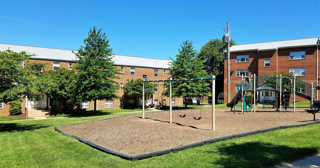 A playground with a swing set and a slide in front of a brick building.