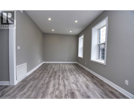 A spacious room with wooden flooring and two windows.