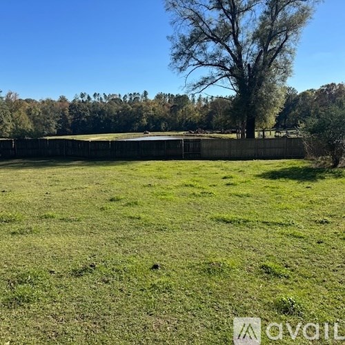 A grassy field with a fence and trees in the distance.