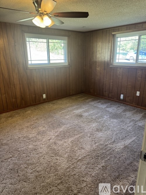 A room with a ceiling fan and two windows.