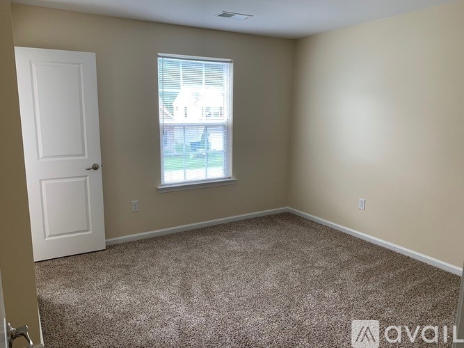 A room with a carpeted floor, a window, and a door.