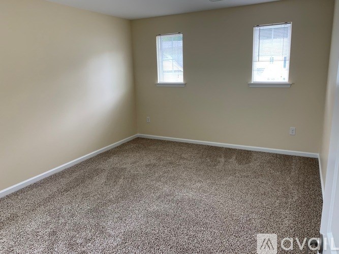 A room with carpeted floor and two windows.