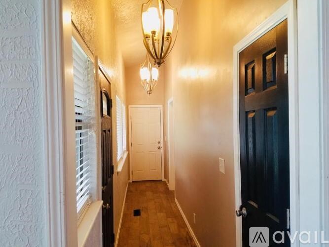 A hallway with a chandelier, two doors, and a window with blinds.