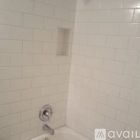 A white tiled shower with a silver faucet.