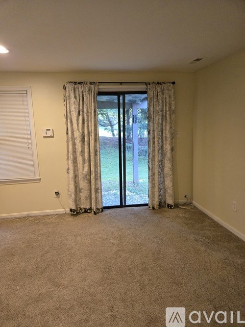 A room with a carpeted floor, a sliding glass door, and a window with closed blinds.
