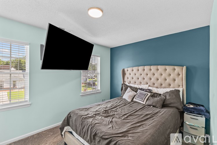 A bedroom with a bed, a window, and a flat screen TV mounted on the wall.