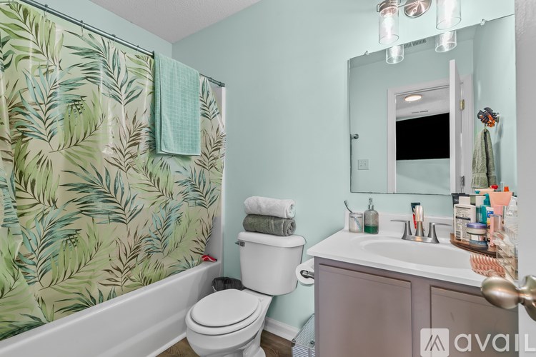 A bathroom with a green leaf patterned shower curtain.