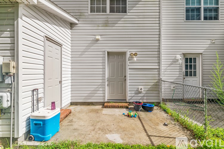 A small backyard with a white house, a blue cooler, and a fence.
