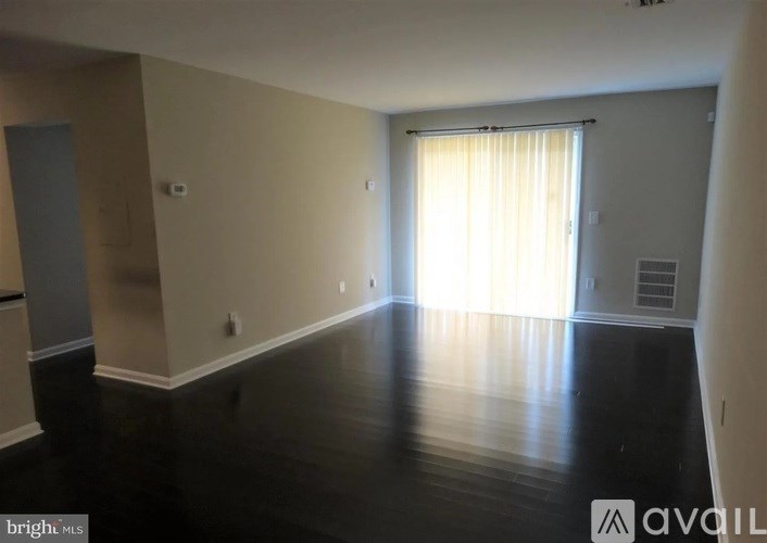 A spacious room with wooden floors and a large window with curtains.