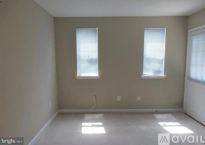 A room with two windows and a white door is available for rent.