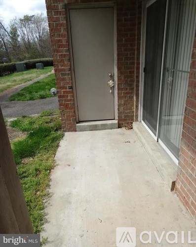 A grey door is on a brick wall with a concrete walkway leading to it.
