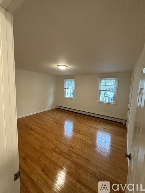 A room with wooden flooring and two windows.