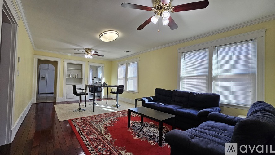A living room with a black couch and a red rug.