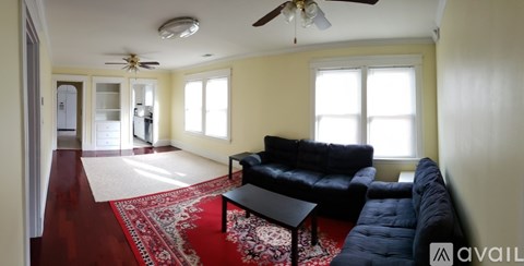A living room with a black couch and a red rug.