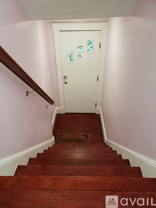 A white door with a glass window is at the end of a wooden staircase.