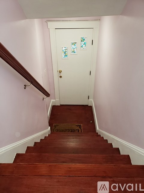 A white door with a glass window is at the end of a wooden staircase.