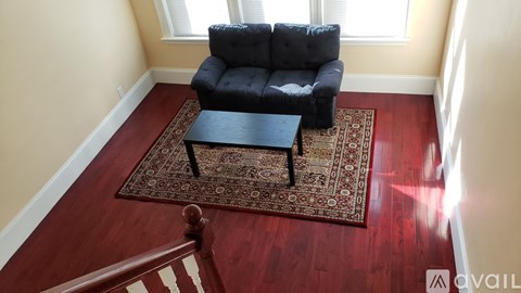 A black leather sofa with a wooden coffee table in front of a rug in a room with wooden floors and windows.