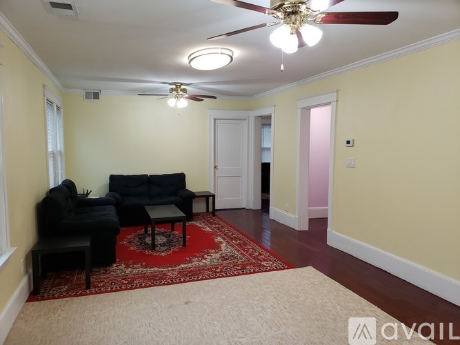 A living room with a black couch and a red rug.