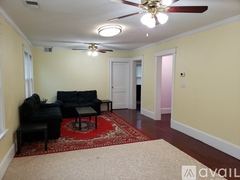 A living room with a black couch and a red rug.
