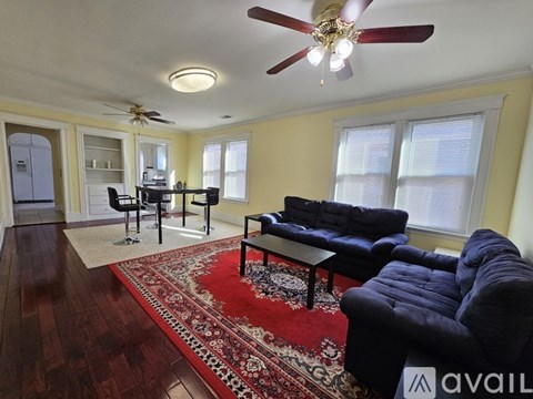 A black sectional sofa with a coffee table in front of a red rug.
