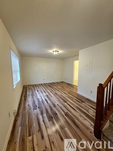 A room with wooden flooring and a window on the left side.