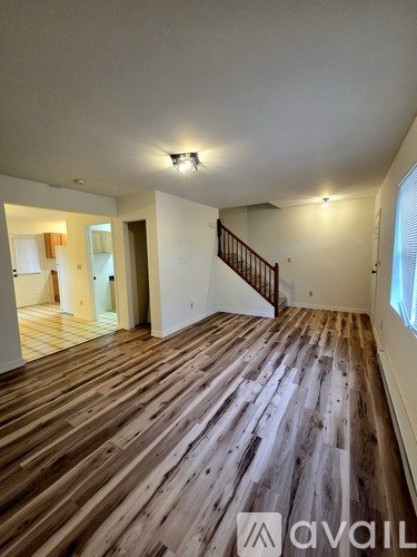 A spacious room with wooden flooring and a staircase.