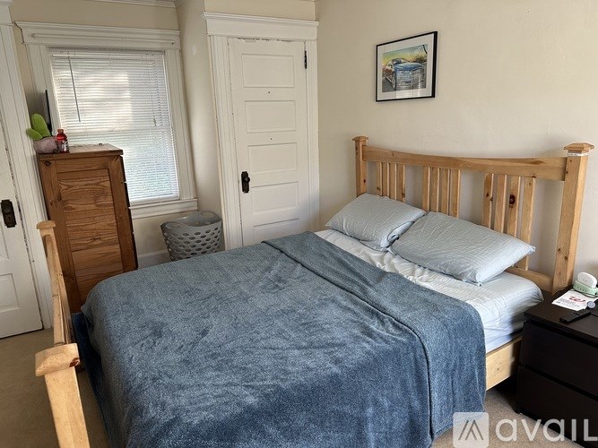 A bed with a blue blanket is in the foreground of a room with a wooden dresser and a white door.