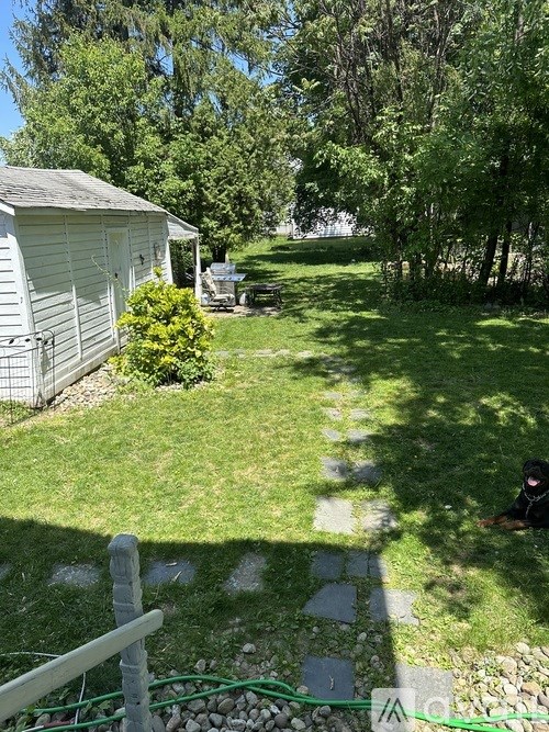 A backyard with a small house, a lawn, and a person sitting on the ground.