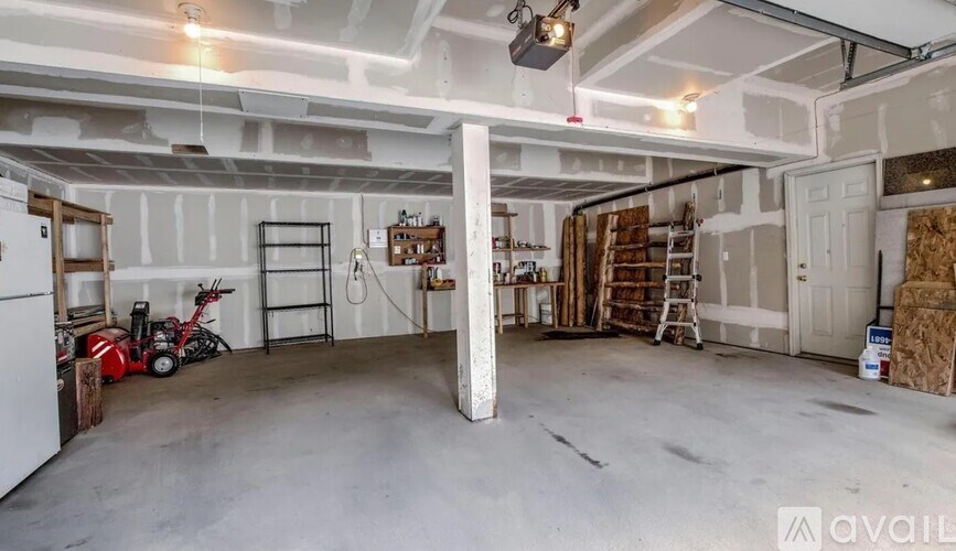 A large, empty garage with a white refrigerator and a red lawn mower.