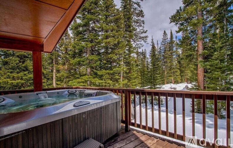 A hot tub sits on a wooden deck with a snowy mountain in the background.