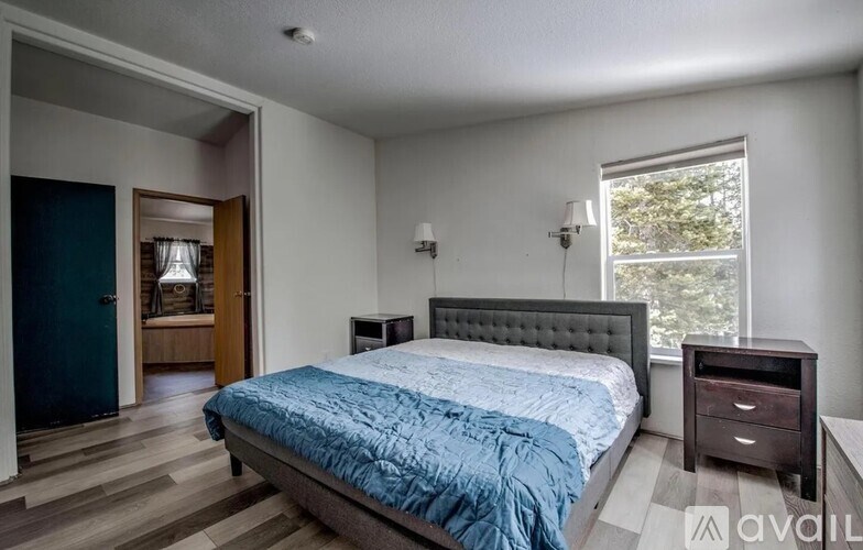 A bedroom with a bed, nightstand, and a window with a view of trees.