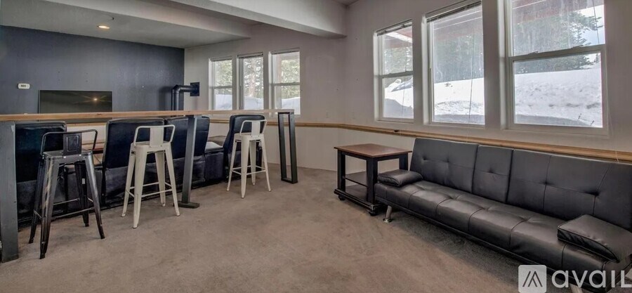 A living room with a grey couch, a wooden table, and a bar area with stools.