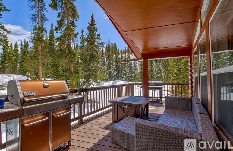 A wooden deck with a grill and seating area overlooking a forest.