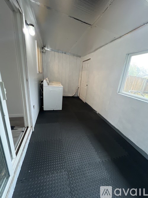 A white washing machine sits in a narrow room with a black floor and white walls.