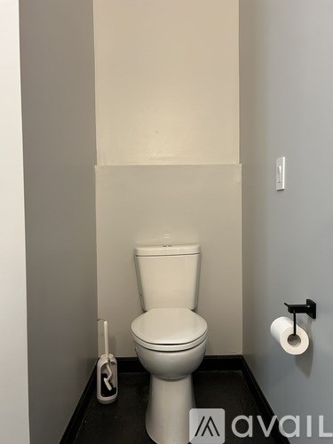 A white toilet in a small bathroom with a roll of toilet paper on the wall.