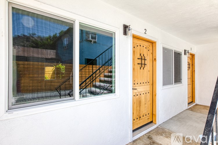 A white wall with a wooden door and a window with a view of a backyard.