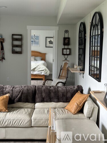 A living room with a grey couch and a bed in the background.
