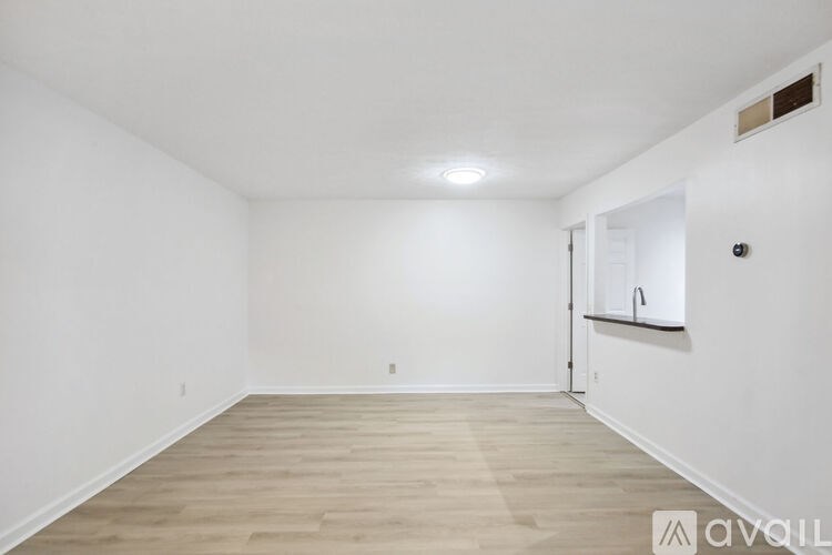 A spacious empty room with wooden flooring and white walls.