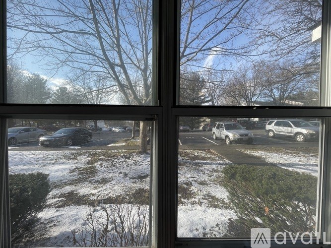 A view of a snowy landscape through a window with cars parked in the background.