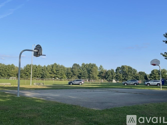 A basketball court with a hoop and a few cars parked in the background.
