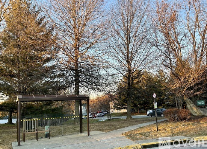 A bus stop with a sign and a tree in the background.