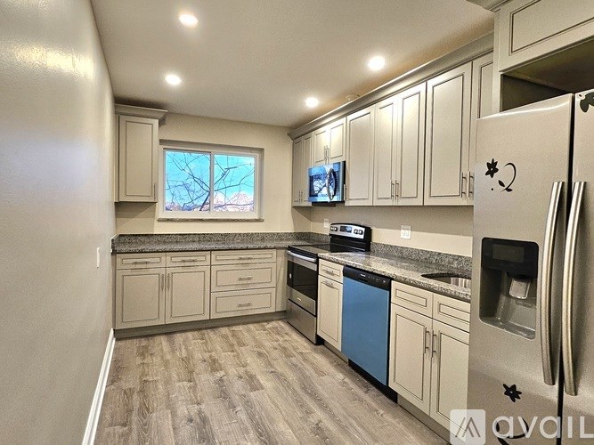 A kitchen with a refrigerator, cabinets, and a window.
