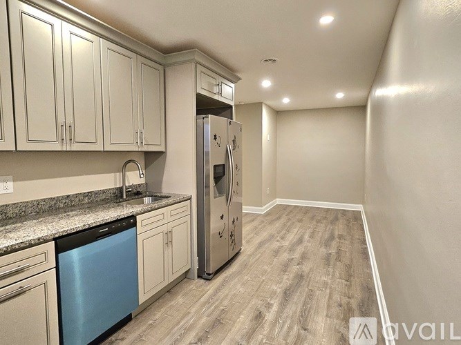A kitchen with a stainless steel refrigerator, a dishwasher, and wooden flooring.