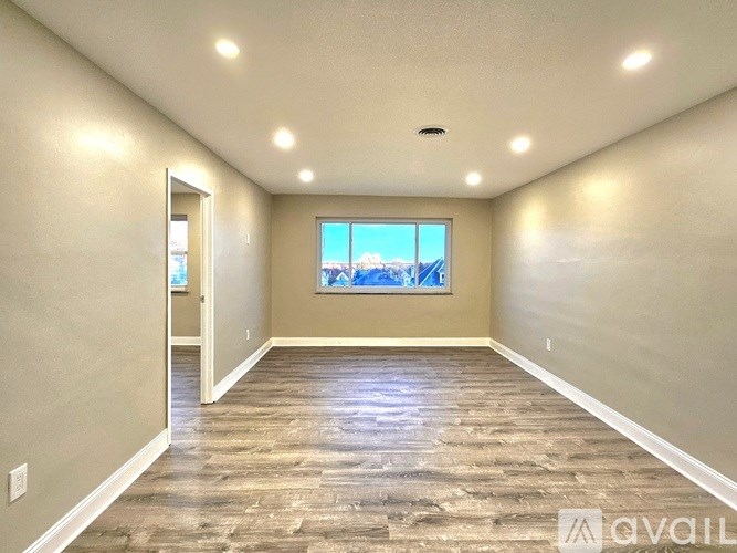 A spacious room with wooden flooring and a large window.