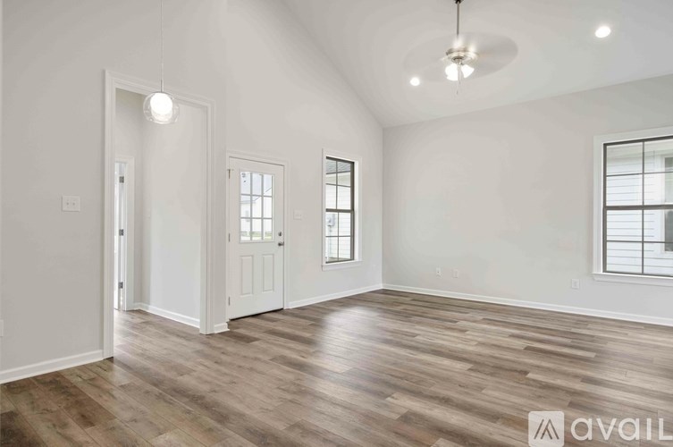 A room with wooden flooring and white walls, with a ceiling fan and three windows.