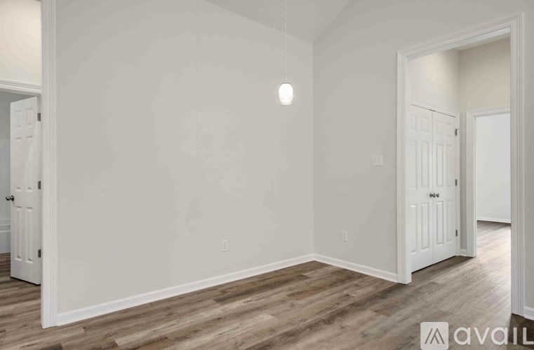 A room with white walls and wooden flooring, with a door on the right and a light on the wall.