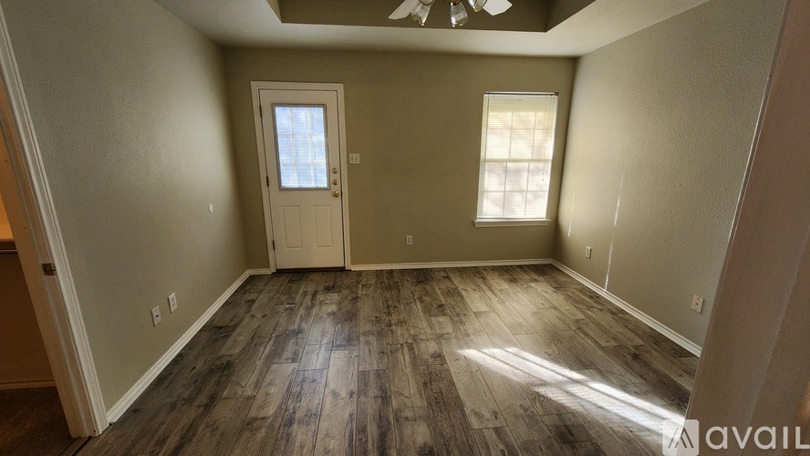 A room with wooden flooring and a door leading to another room.