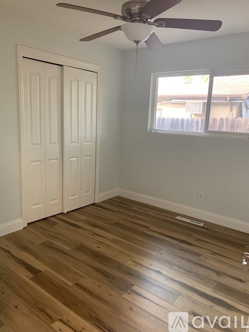 A room with a ceiling fan and a window with a view of a fence.