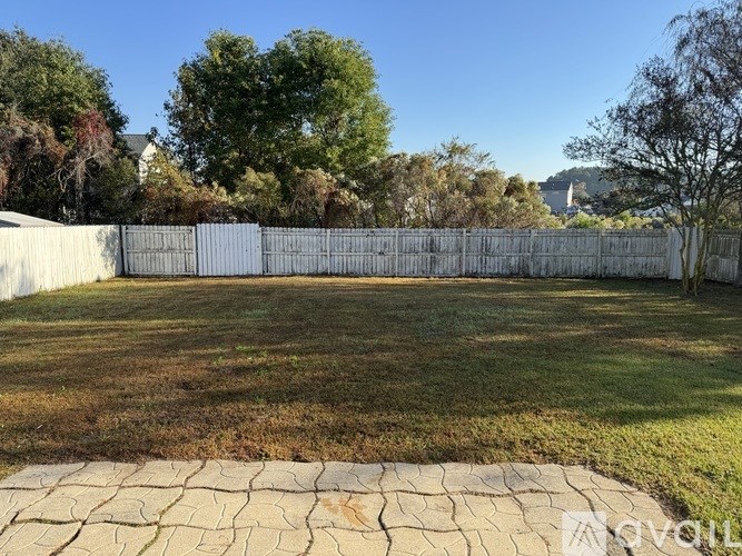 A backyard with a stone patio and a white fence.