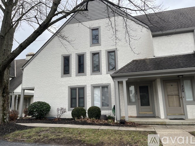 A white house with a grey roof and a tree in front.